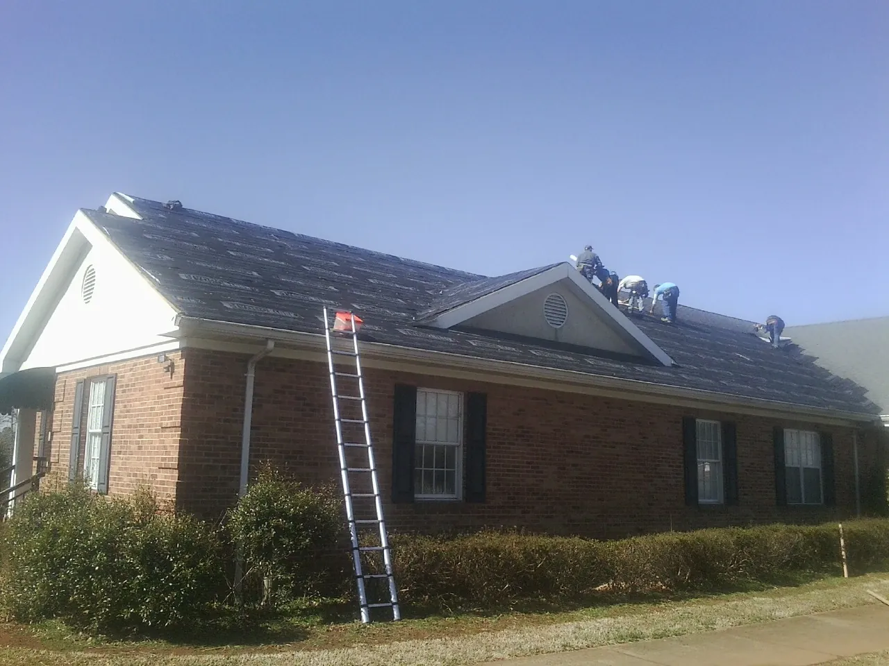 Crew tearing shingles off a brick ranch roof with a ladder set — Metal Roof Repair work by our crew in Windsor