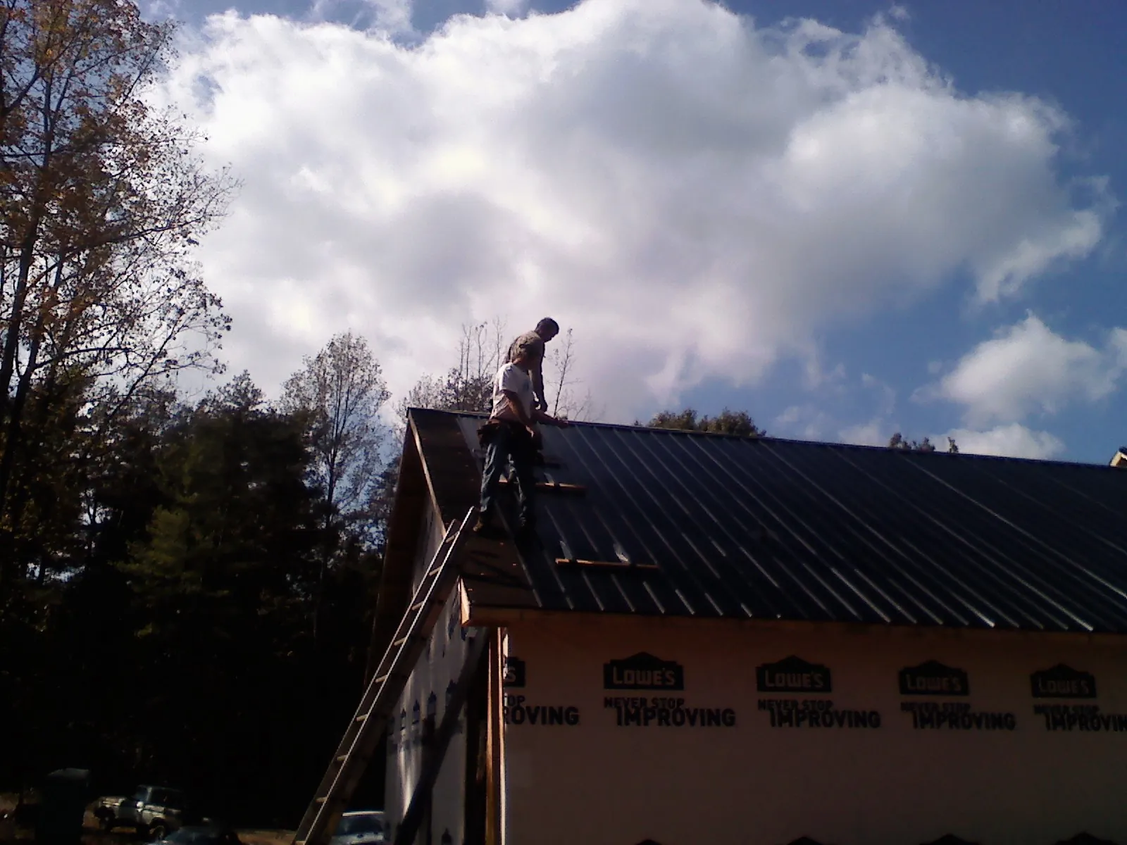 Roofer fastening dark metal panels high against a cloudy sky, from a Roof Inspection job in Windsor